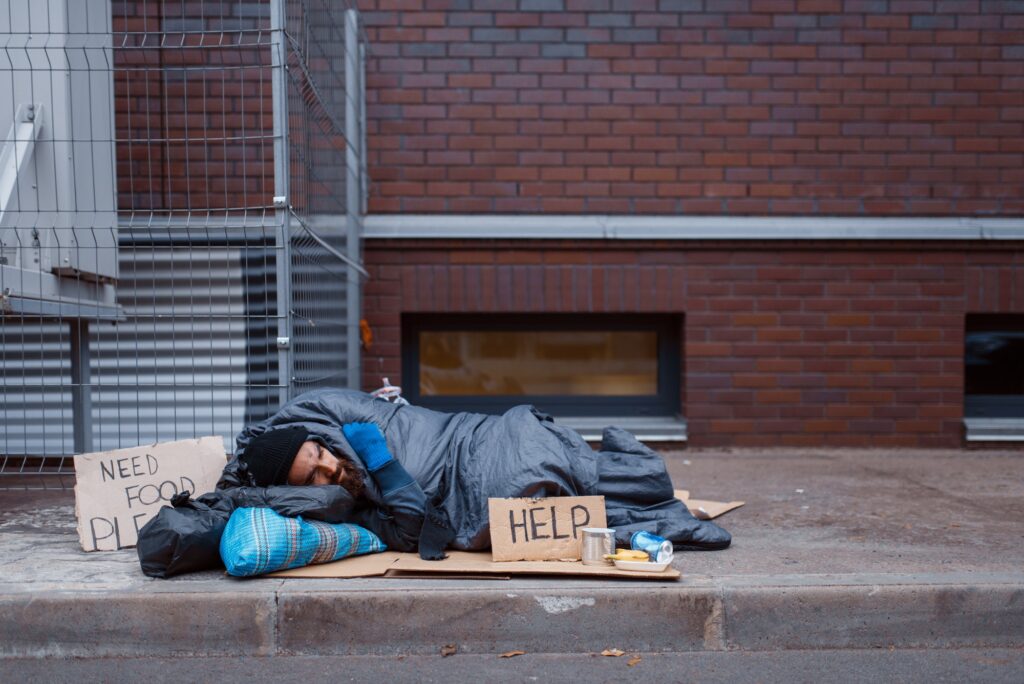 Dirty homeless with help sign lies on city street